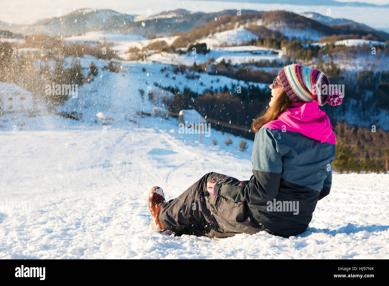 Felice ragazza seduta nella neve sulla cima della montagna Foto Stock