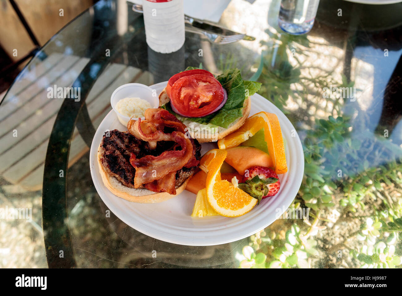 Hamburger con pancetta sulla parte superiore su un soffice focaccia di pane e di un lato della frutta comprese le arance, fragole, meloni e ananassi per l Foto Stock