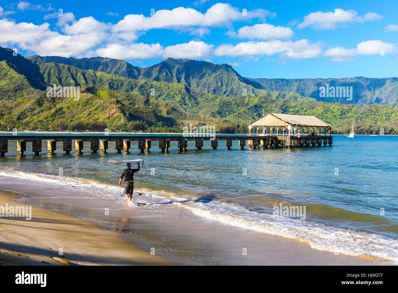 Surfer trasporta le tavole da surf in spiaggia Hanalei vicino al molo di Hanalei su Kauai Foto Stock