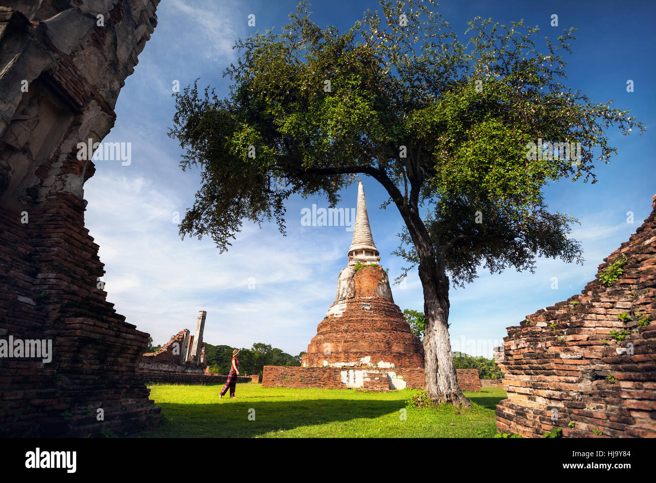 Giovane donna in abiti rosso con fotocamera foto guardando antichi rovinato Wat Mahathat in Ayutthaya, Thailandia Foto Stock