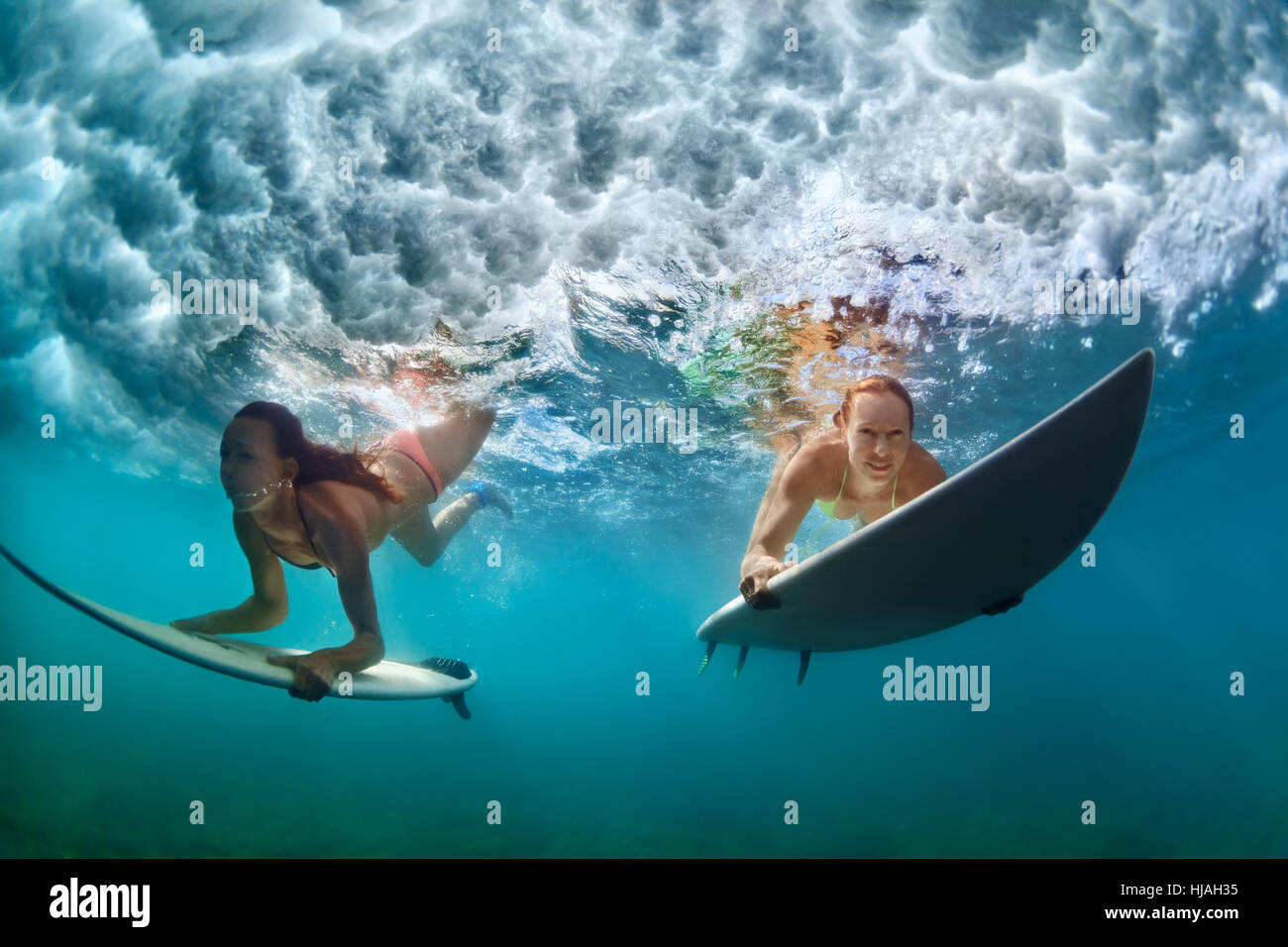 Un gruppo di ragazze attive in azione. Surfer donne con tavola da surf tuffarsi underwater in onda. Sport d'acqua, surf estremo Foto Stock