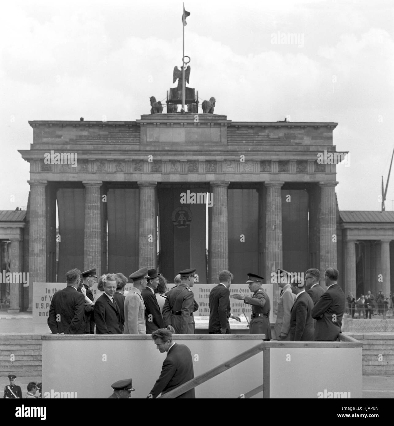 Il presidente statunitense John Fitzgerald Kennedy in corrispondenza di un punto di vista presso il muro di Berlino il 26 giugno 1963. La Porta di Brandeburgo per motivi di easten parte della città divisa è stata coperta con le bandiere rosse. Foto Stock