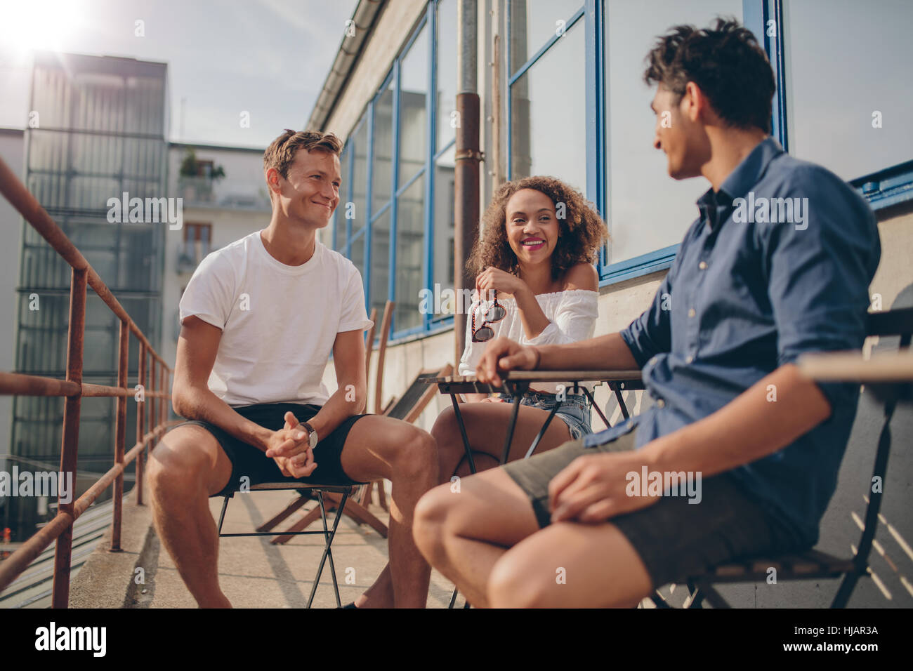 Tre giovani amici insieme a outdoor cafe. Multirazziale del gruppo di giovani persone sedute intorno ad un piccolo tavolo del bar chiacchierando e sorridente. Foto Stock