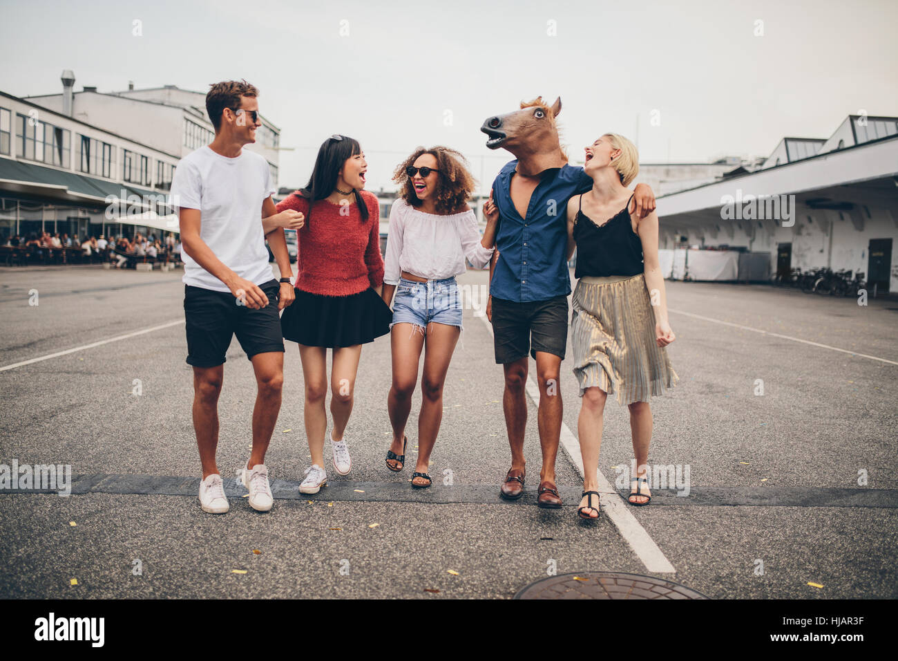 A piena lunghezza shot di multirazziale giovani amici divertendosi insieme sulla strada. Un gruppo di giovani uomini e donne a piedi all'aperto, con un uomo che indossa h Foto Stock A piena lunghezza shot di multirazziale giovani amici divertendosi insieme sulla strada. Un gruppo di giovani uomini e donne a piedi all'aperto, con un uomo che indossa h Foto Stock
