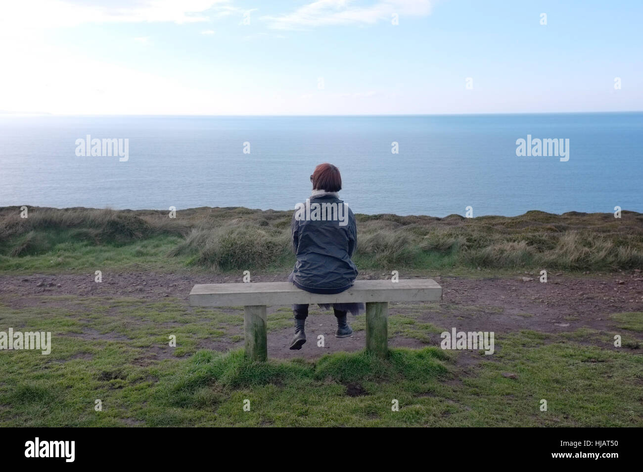 Una donna seduta su una panchina vicino Wheal Coates, Cornwall. Foto Stock