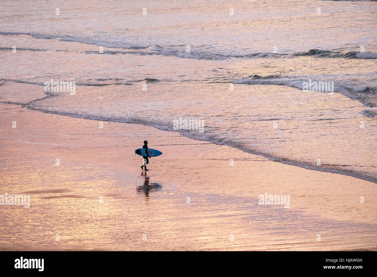 Un surfista passeggiate in mare mentre il sole tramonta su Fistral Beach in Newquay, Cornwall, Inghilterra. Foto Stock