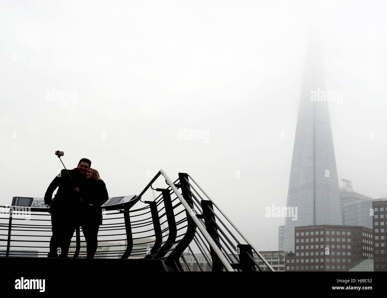 Un paio di prendere un 'selfie' sul Tamigi percorso tramite il ponte di Londra con la Shard avvolta nella nebbia dietro di loro, come nebbia fitta causato interruzioni di viaggio attraverso il sud dell'Inghilterra, con migliaia di passeggeri aerei rivolta verso le cancellazioni e ritardi. Foto Stock