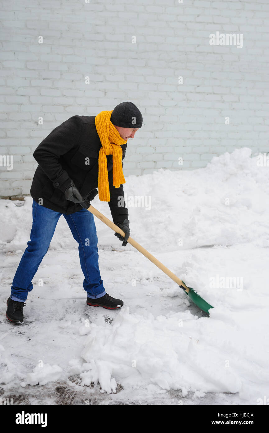 Uomo in un foulard arancione pulisce la neve Foto Stock