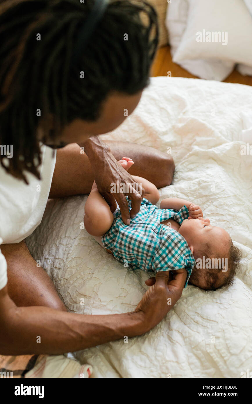 Padre vestire il bambino a letto Foto Stock