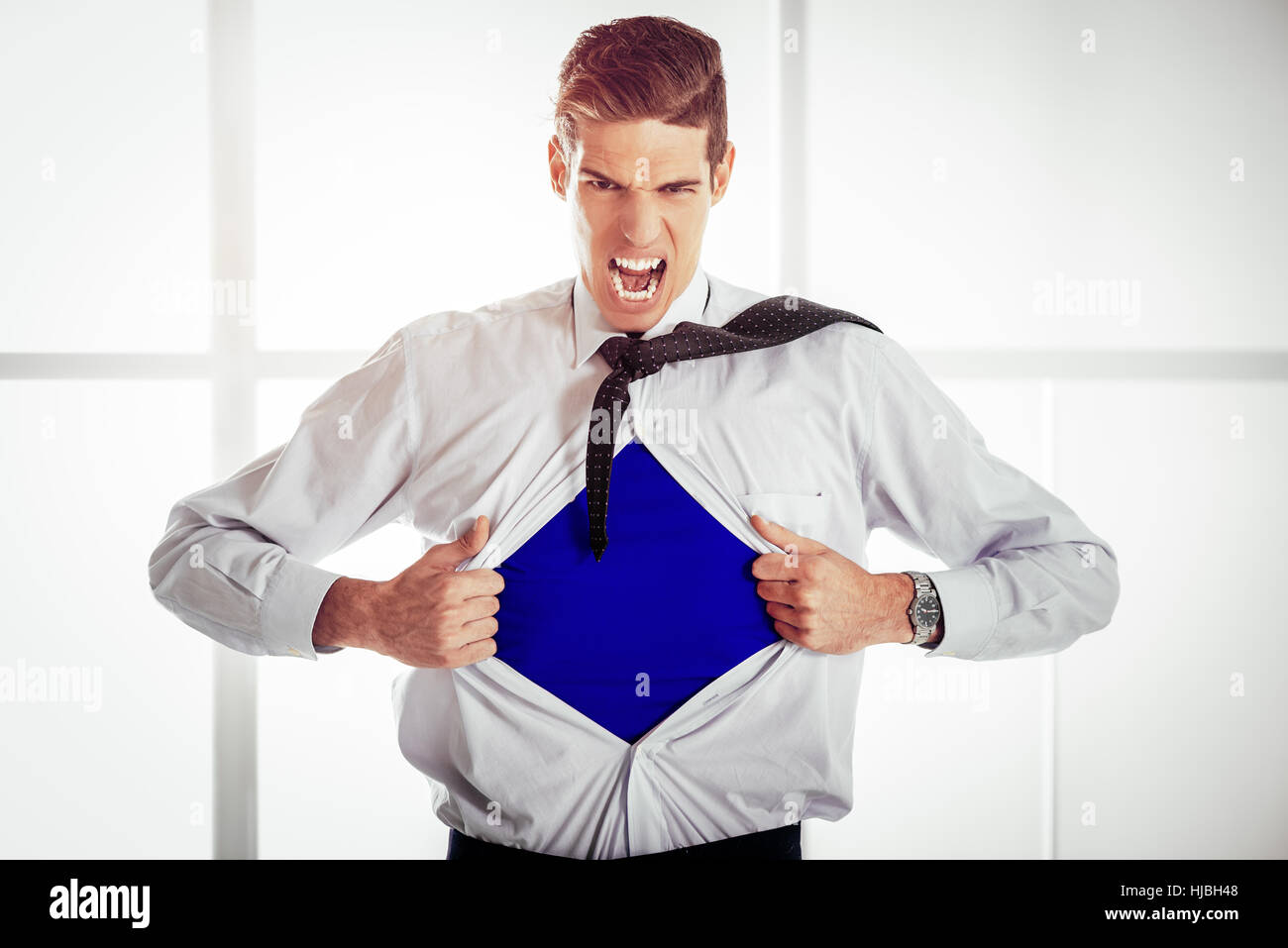 Imprenditore arrabbiato strappando aprire la sua maglietta e esponendo un supereroe costume blu al di sotto. Guardando alla fotocamera. Foto Stock