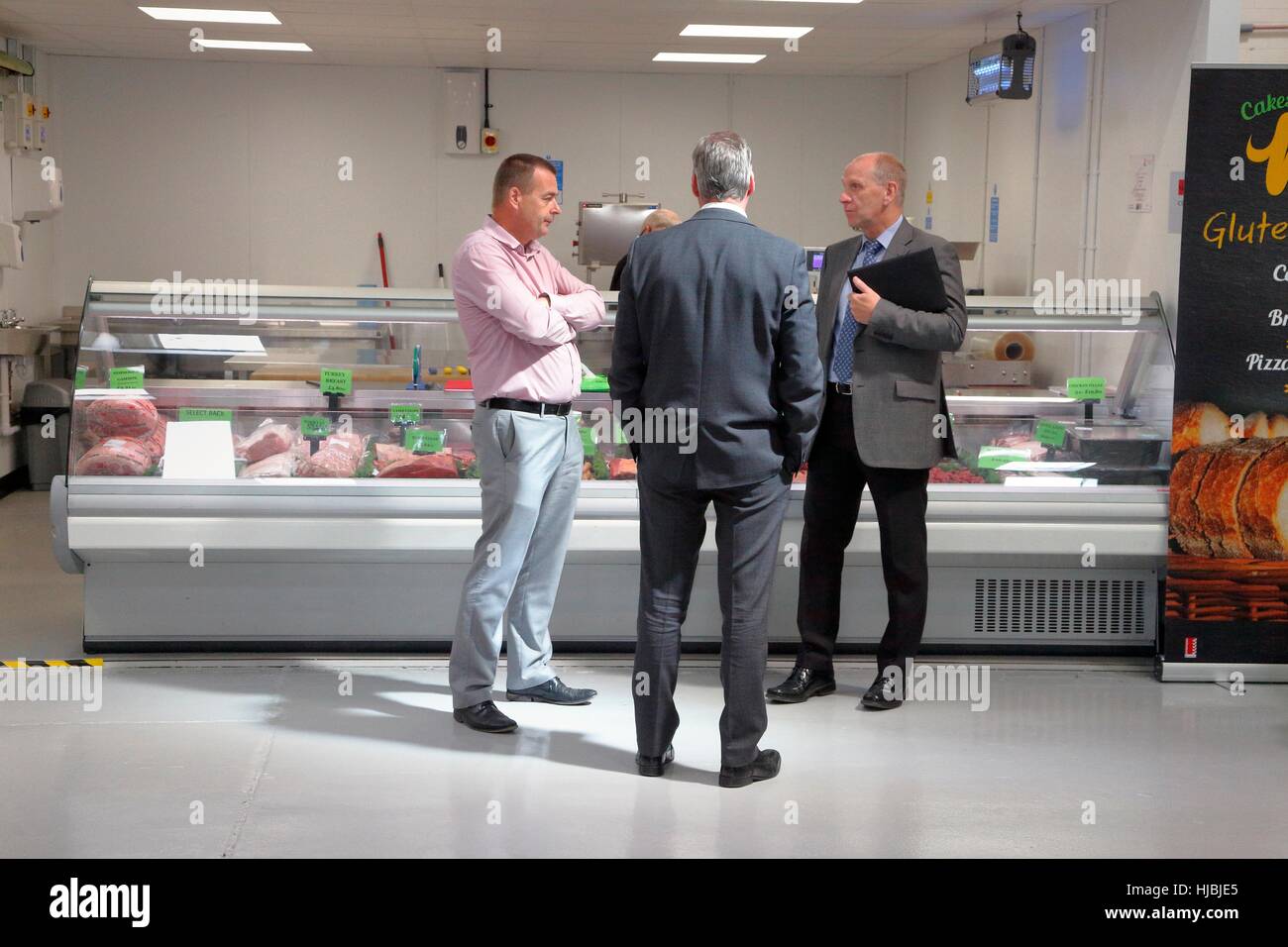 Tre uomini in chat nella parte anteriore della macelleria sezione di un grossista di prodotti alimentari. Foto Stock