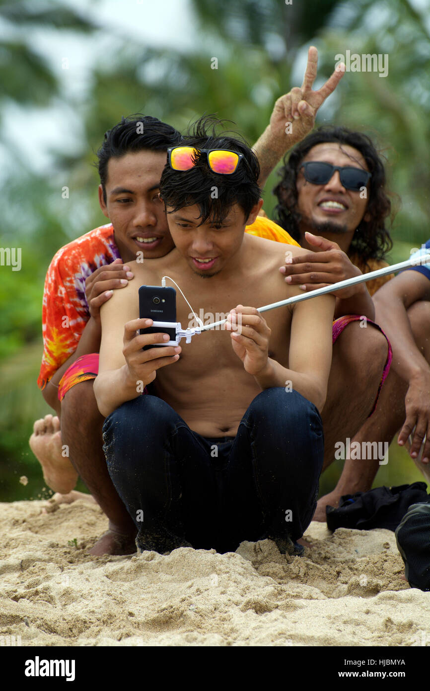 Simpatico gruppo di giovani uomini Balinese poise per selfie foto con selfie stick mostra giovani cool ride, sorrisi e calore Foto Stock