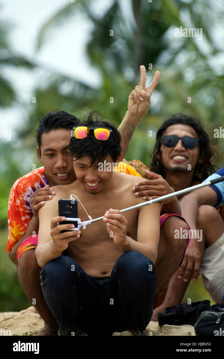 Simpatico gruppo di giovani uomini Balinese poise per selfie foto con selfie stick mostra giovani cool ride, sorrisi e calore Foto Stock