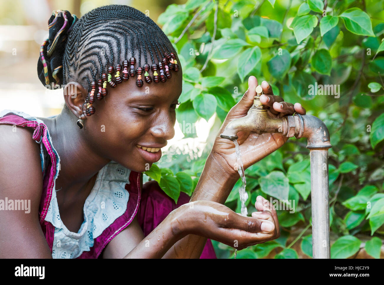 Felice African Schoolgirl godendo di acqua pulita da un rubinetto di Bamako, in Mali Foto Stock