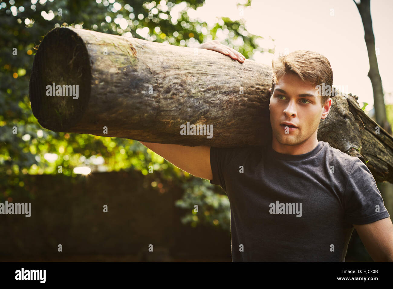 Ritratto di giovane uomo della formazione, sollevamento tronco di albero in spalla in posizione di parcheggio Foto Stock