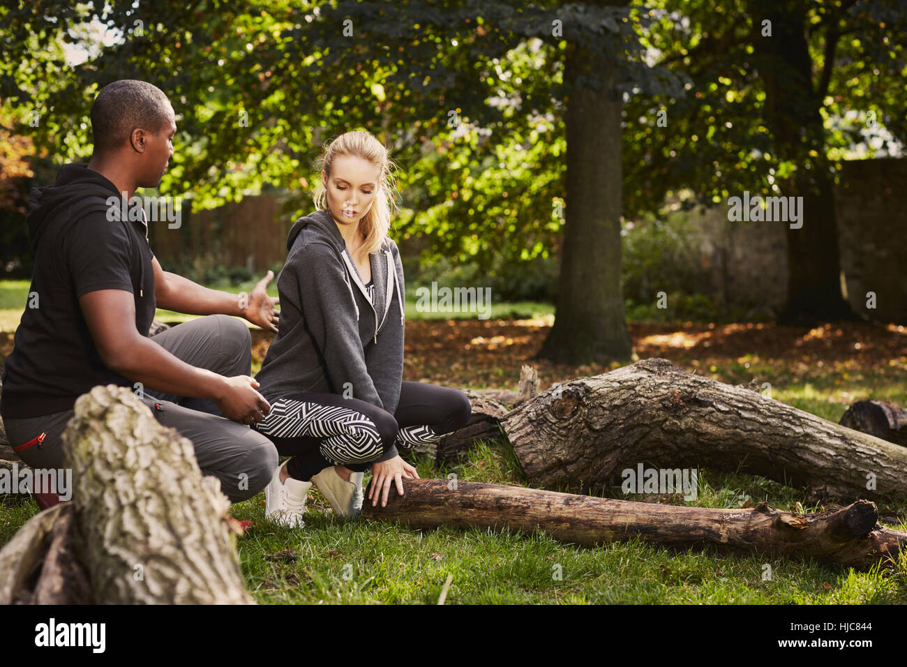 Personal trainer che mostra giovane donna come per sollevare il tronco di albero in posizione di parcheggio Foto Stock