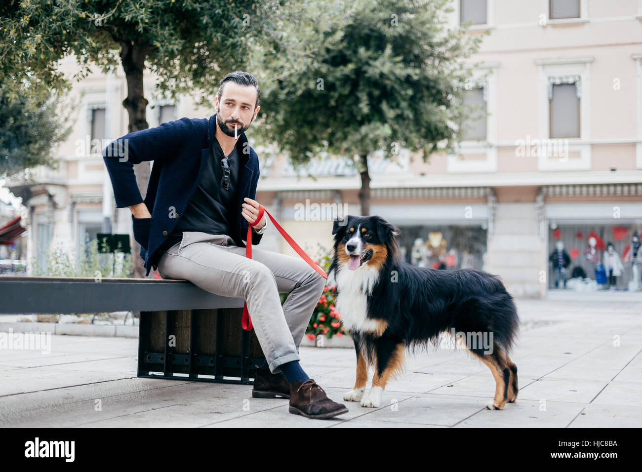 Uomo con cane Sigaretta fumare sulla strada di città panchina Foto Stock