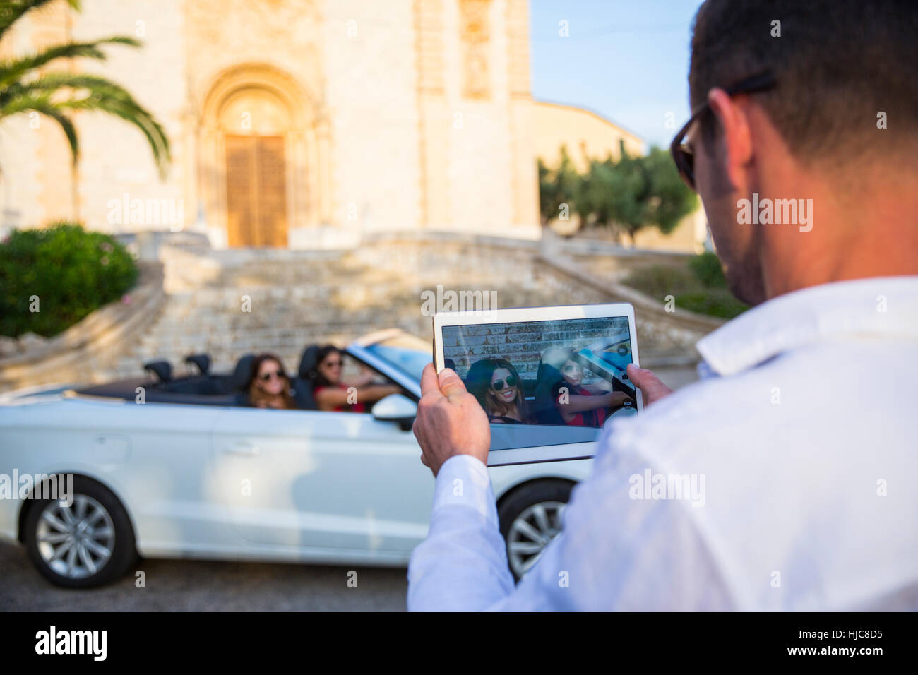 Sulla spalla dell'uomo fotografare due giovani donne turisti nel convertibile, Calvia, Maiorca, SPAGNA Foto Stock