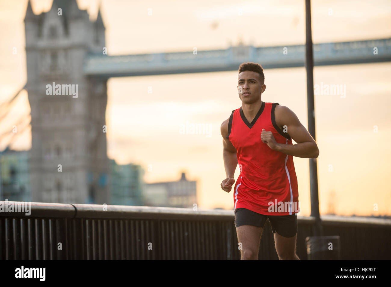 Uomo che corre da Riverside, Tower Bridge in background, Wapping, London, Regno Unito Foto Stock