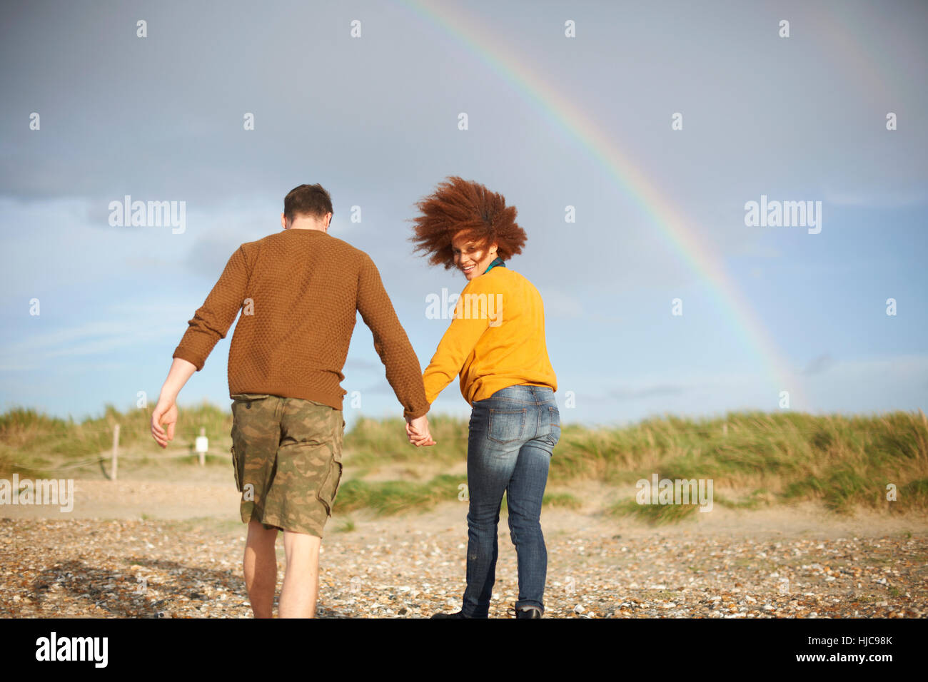 Giovane camminando sulla spiaggia verso rainbow Foto Stock