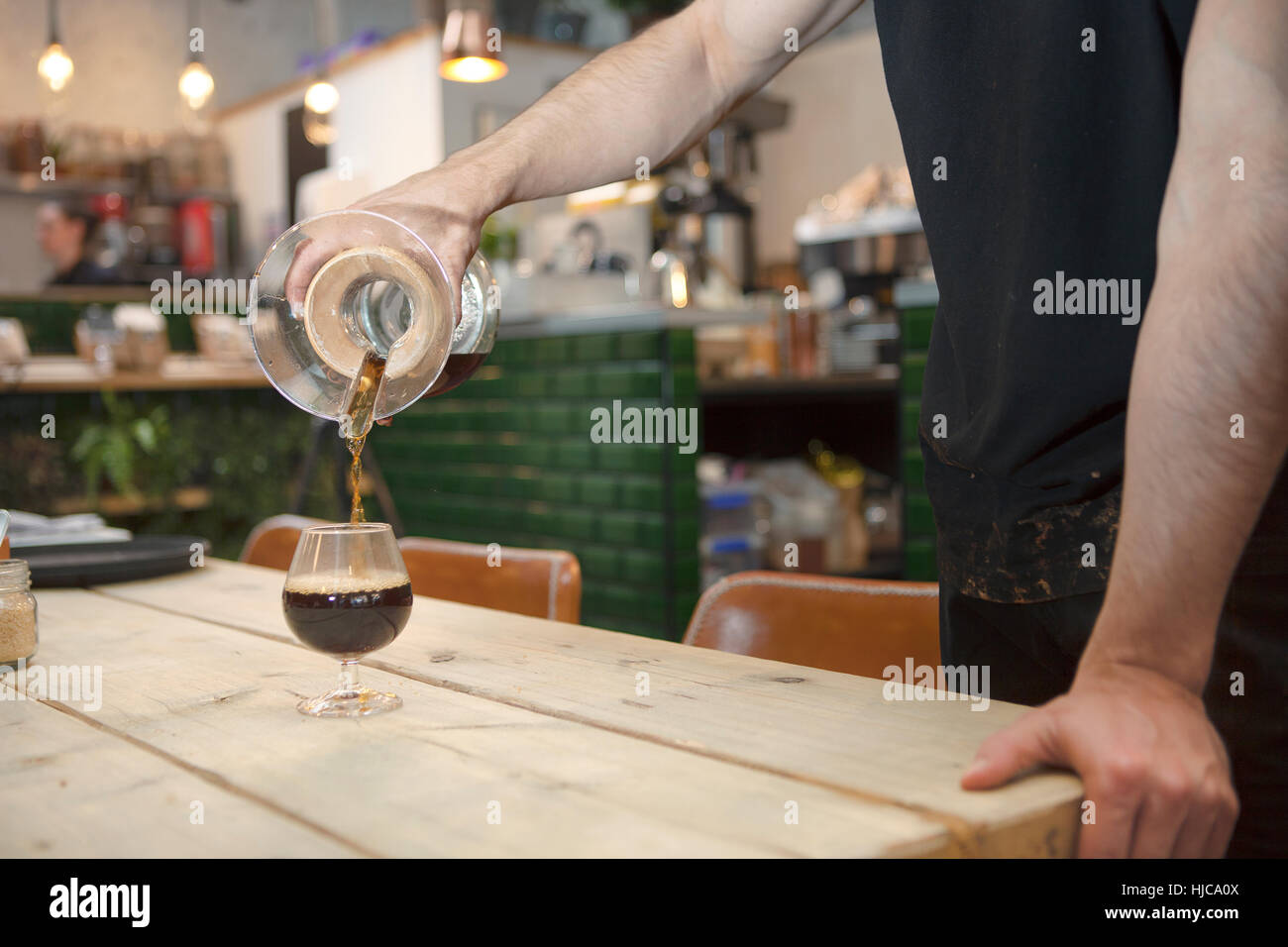 Barista maschio con le mani in mano versando il caffè nero in acquavite di vetro in cafe Foto Stock