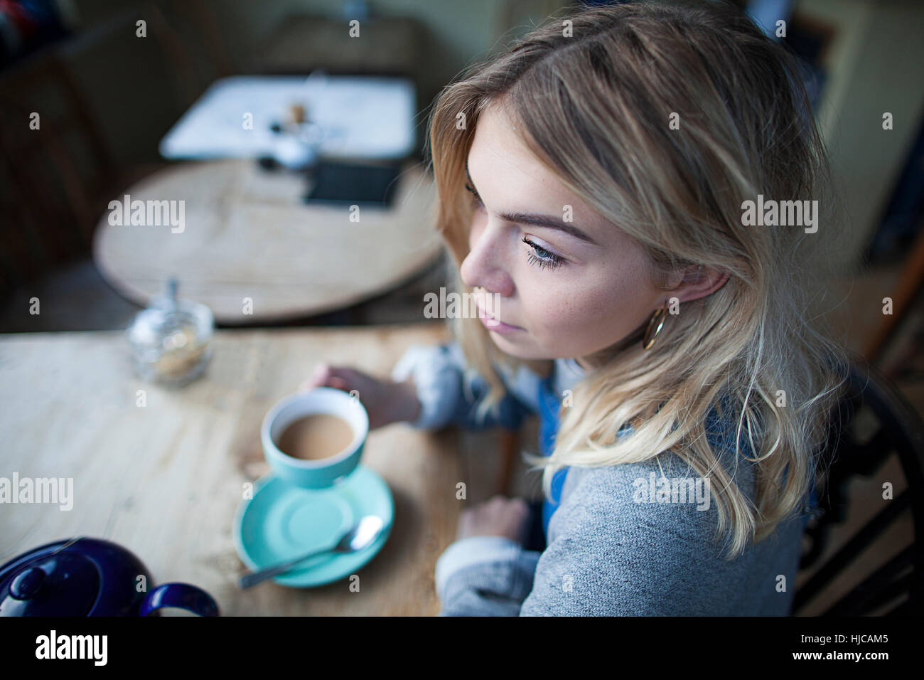 Giovane donna seduta al cafe, tenendo tazza da tè, riflessivo espressione sul viso Foto Stock