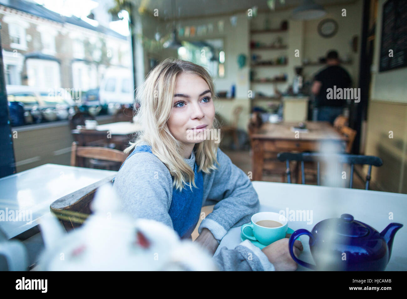 Giovane donna seduta al cafe, guardando fuori della finestra Foto Stock