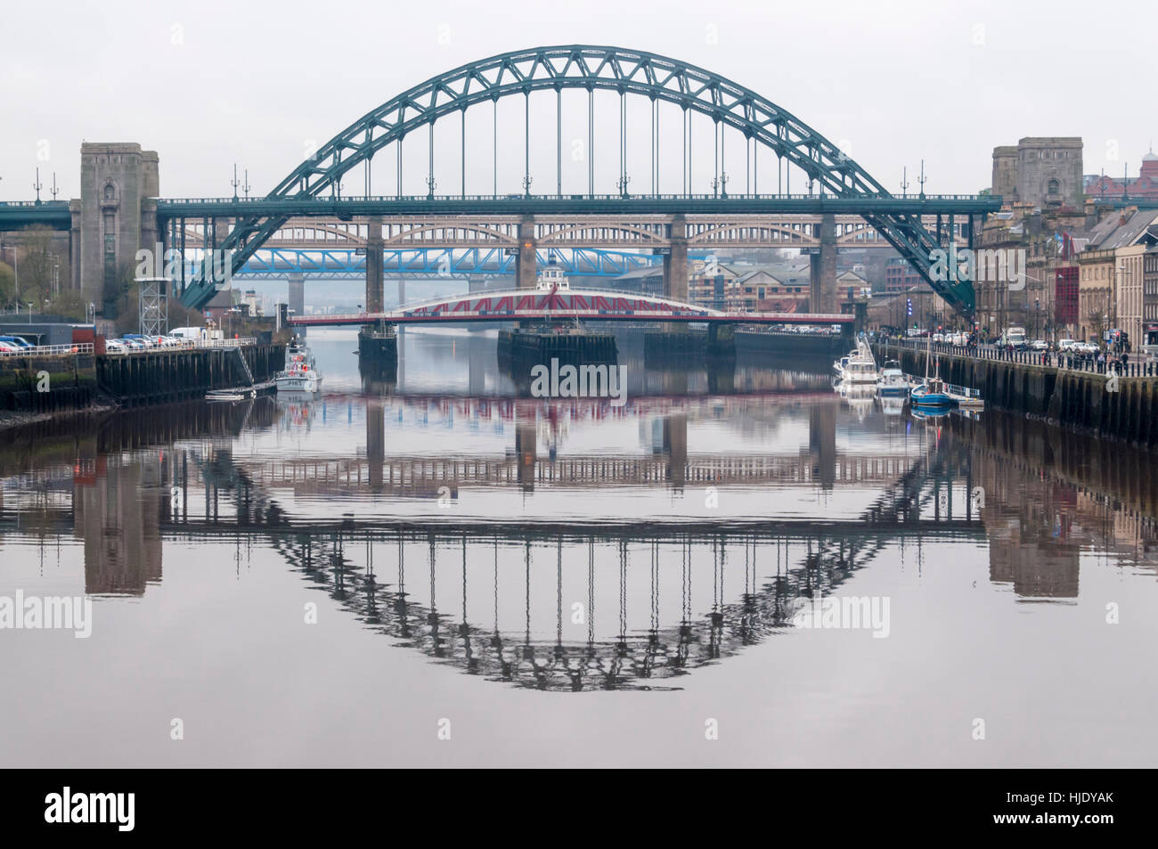 Il Tyne Bridge e bridge ad alto livello si riflette nelle calme acque del Fiume Tyne a Newcastle Upon Tyne, Inghilterra, Regno Unito. Foto Stock