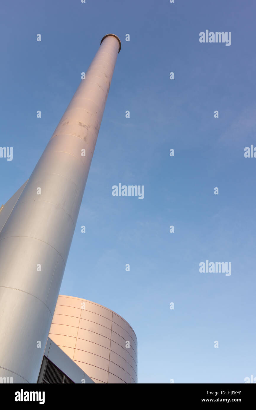Cisterna di olio e il camino a termal power plant. Un alto chimneypot contro il cielo blu Foto Stock
