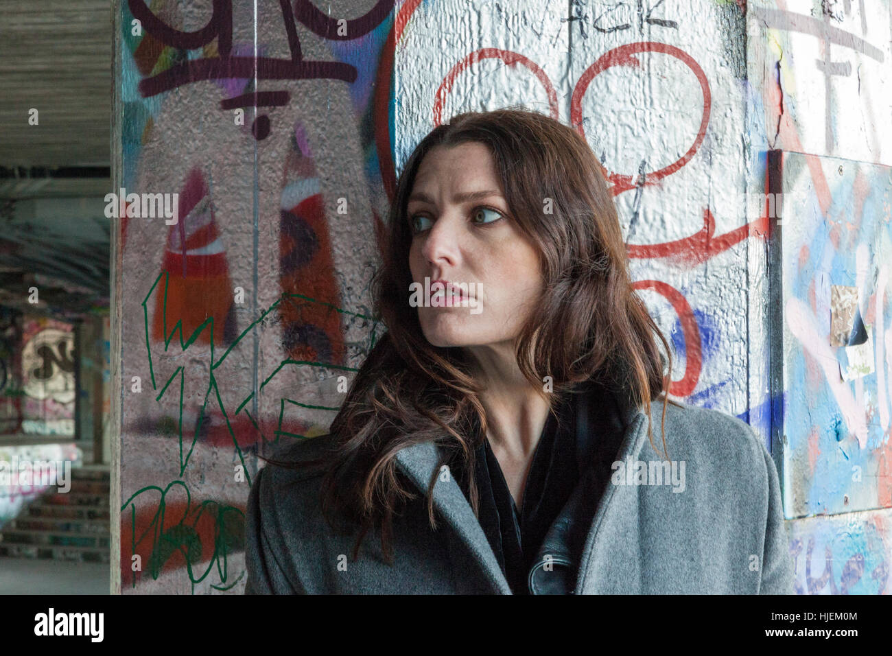 Attraente dai capelli scuri donna nascosto dietro una coperta di graffiti pilastro Foto Stock