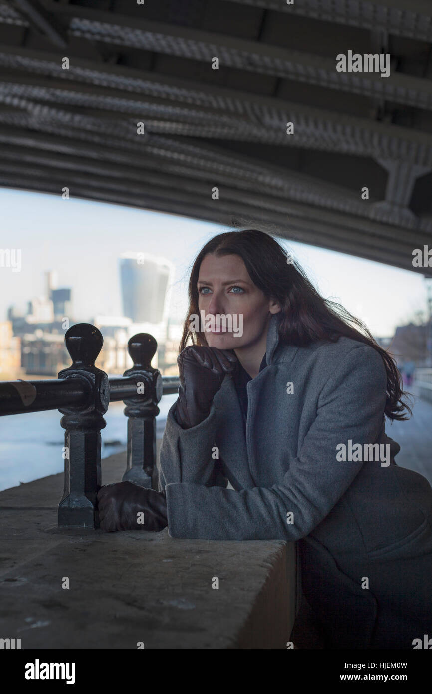 Attraente dai capelli scuri donna alla ricerca tesa e ansiosa guarda fuori da sotto un ponte in un contesto urbano Foto Stock