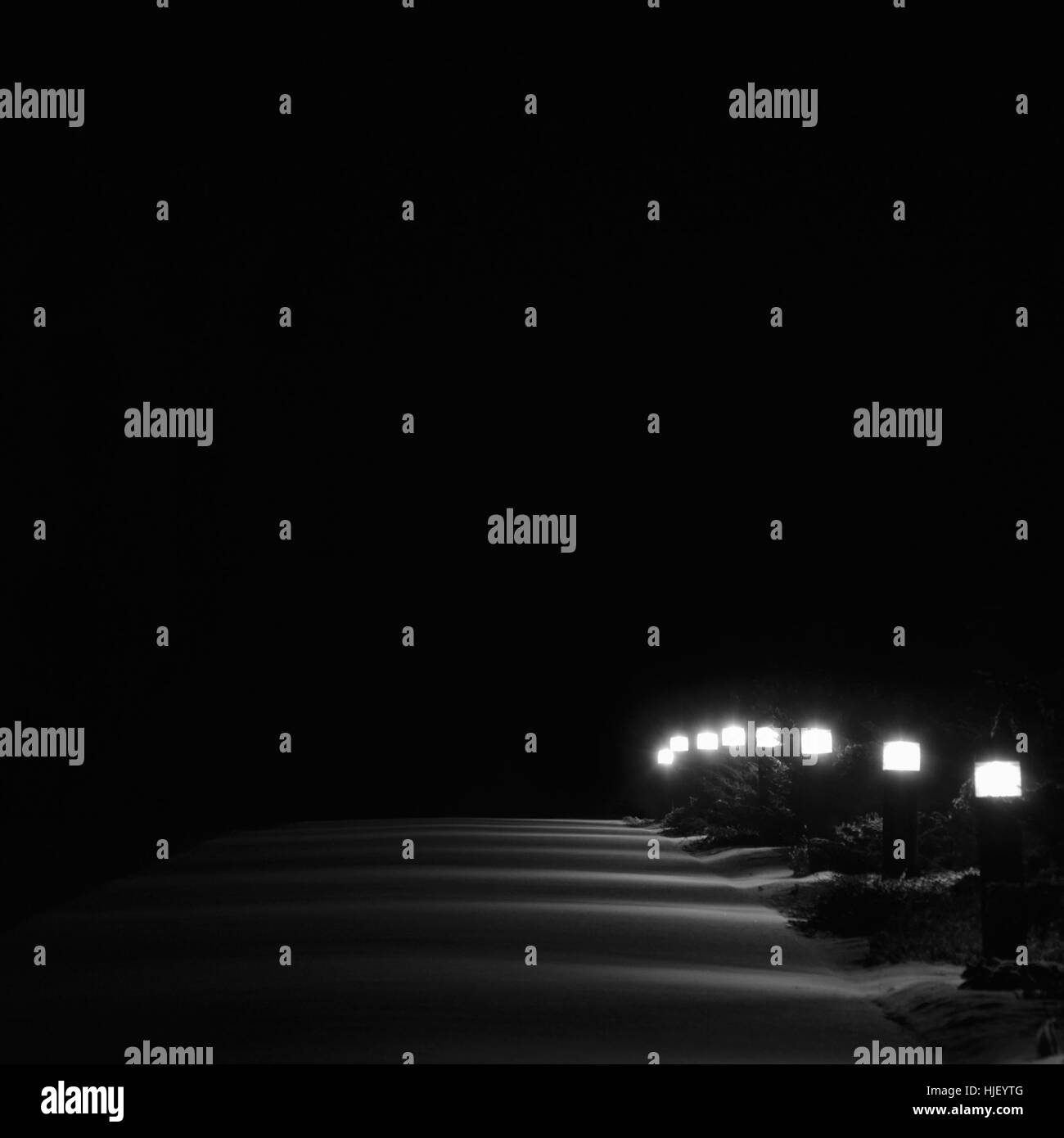 Illuminato parco innevato sentiero, luci luminose accese bianco percorso Outdoor pavimentazione lanterne lampioni prospettiva di riga di notte, prima neve invernale Foto Stock