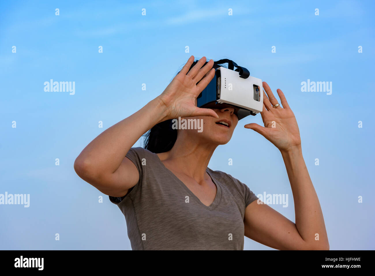 Sorpresa la donna (in 40s) indossando una realtà virtuale auricolare (VR) di maschera con il cielo a poche nuvole dietro di lei. Foto Stock