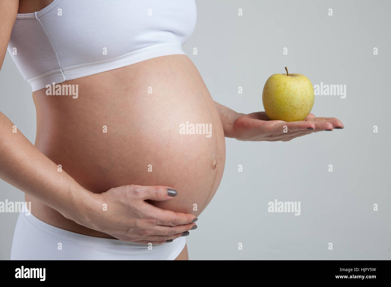 La pancia di una donna incinta con mela verde sulla sua mano Foto Stock