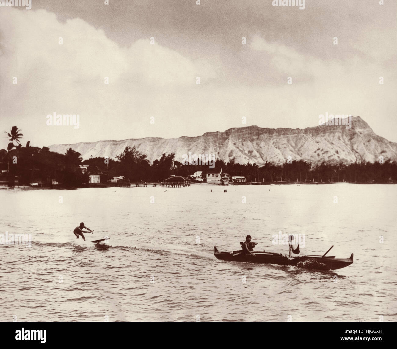 Canoa Outrigger il traino di un surfista nell'oceano di Waikiki a Honolulu, Hawaii nel 1930. Foto Stock