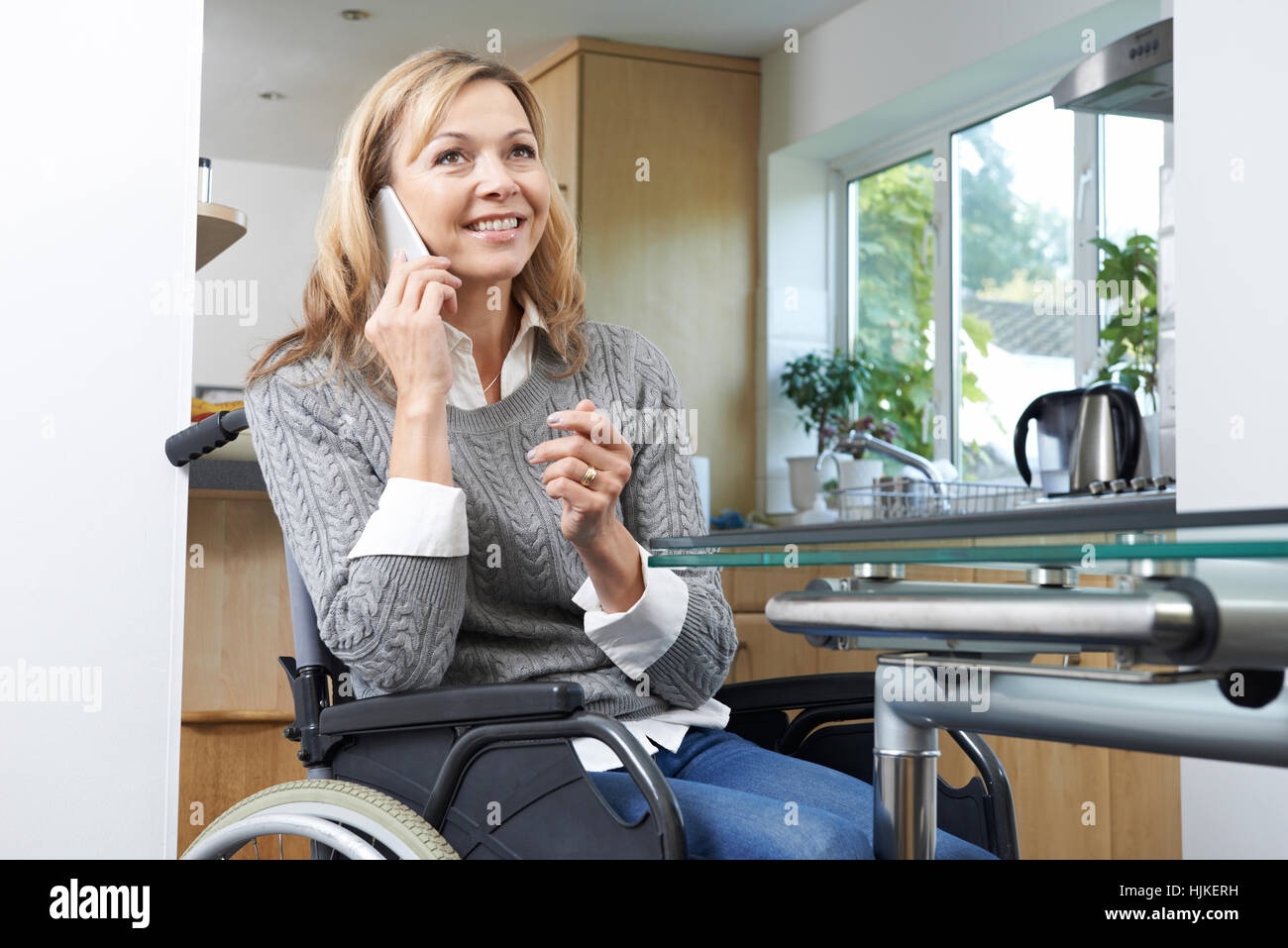 Donna disabile in carrozzella effettuare una chiamata sul telefono cellulare a casa Foto Stock