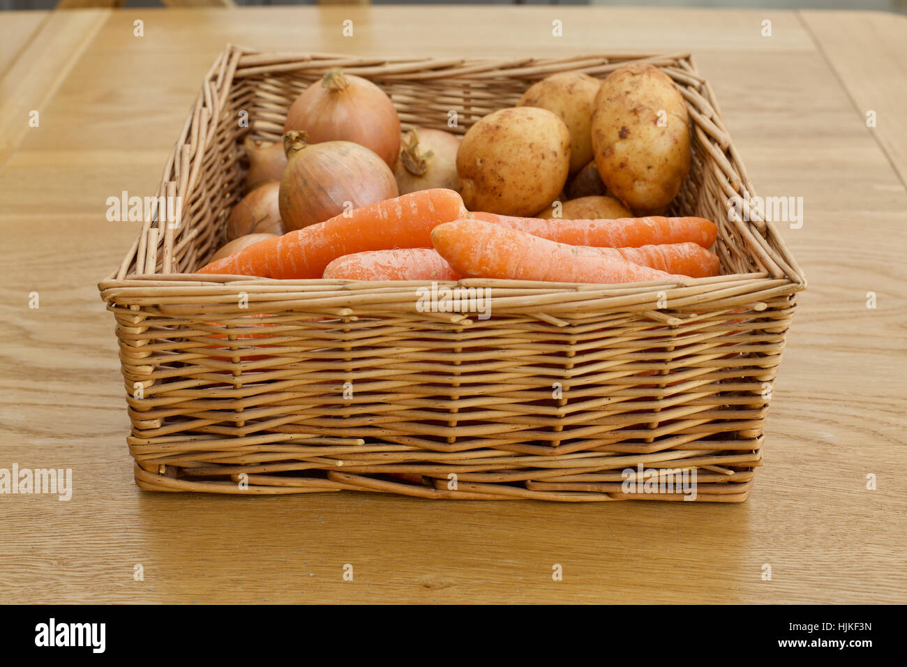 Cesto di verdure carote cipolle patate su una tavola di legno Foto Stock