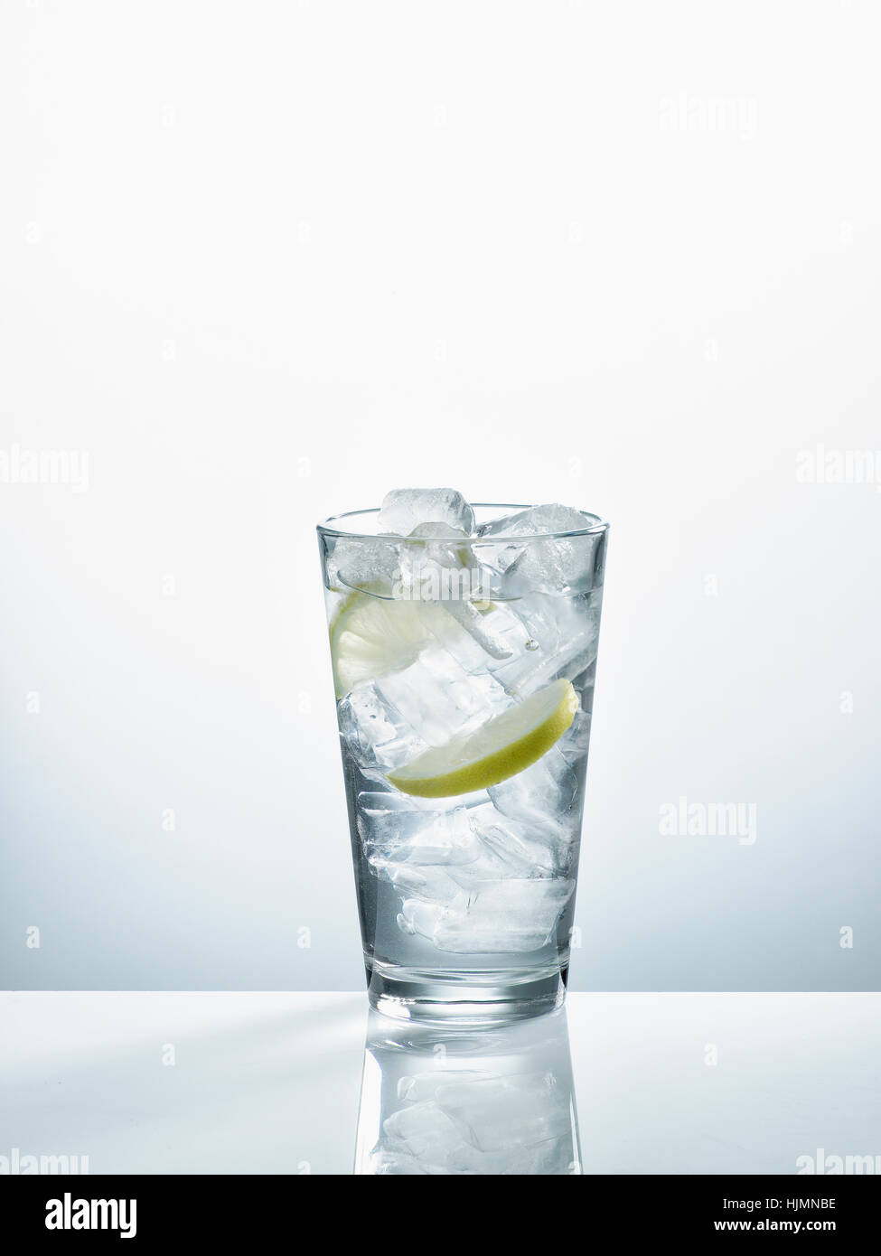 Vetro con acqua minerale, cubetti di ghiaccio e fettine di limone davanti a uno sfondo bianco Foto Stock