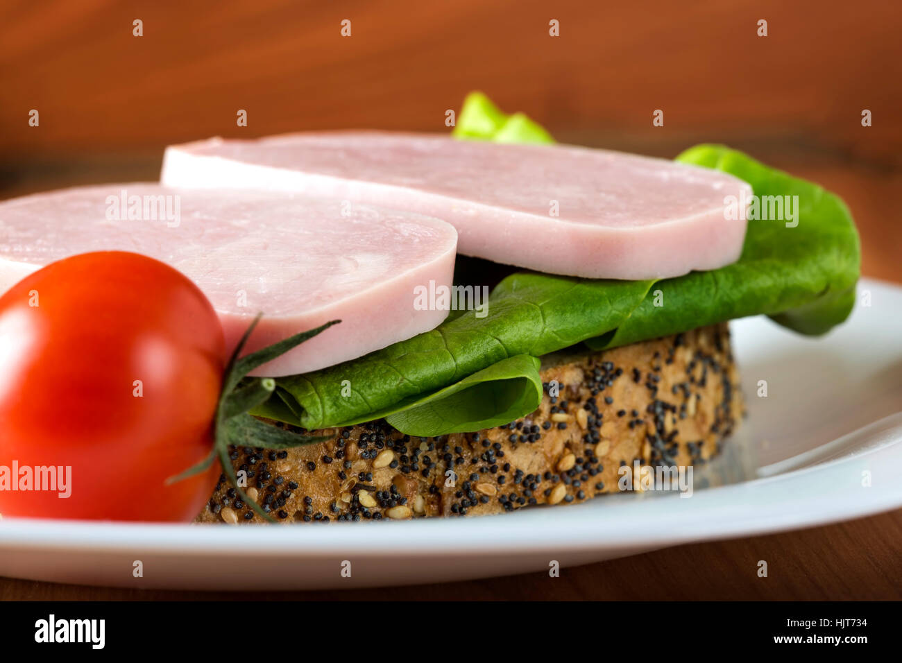 Aprire il panino con prosciutto, insalata verde e un pomodoro sulla piastra bianca Foto Stock