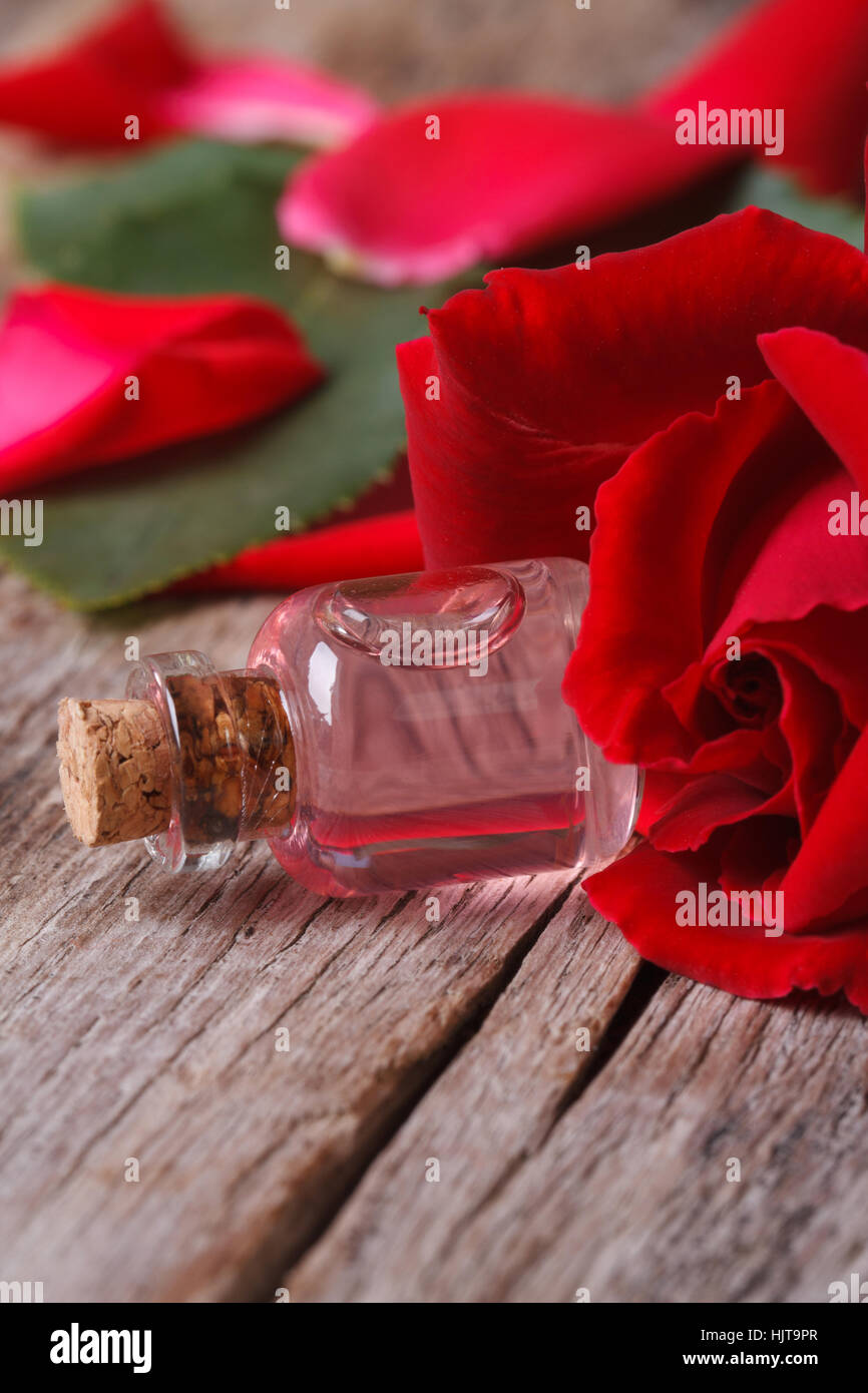 Bottiglia di acqua di rose e rose rosse su una tavola di legno verticale. close up Foto Stock