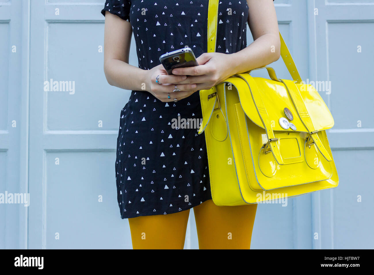 Giovane femmina caucasica con portamonete giallo tenendo lo smartphone Foto Stock