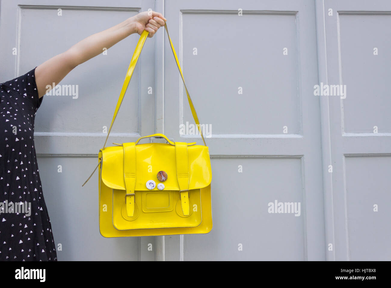 Giovani caucasici azienda femmina giallo purse contro uno sfondo grigio Foto Stock