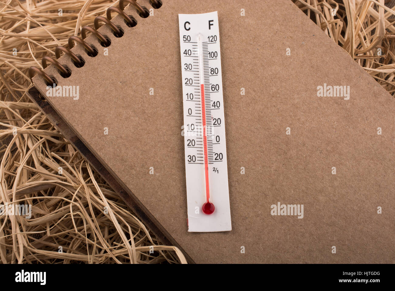 Termometro su un notebook marrone su un sfondo di paglia Foto Stock