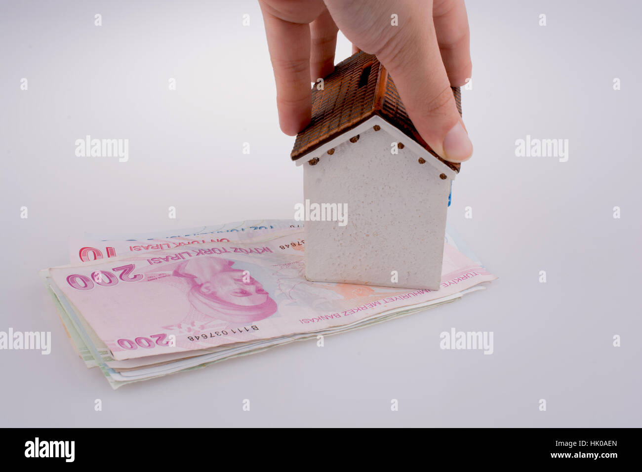 Mano che regge un modello di casa dal lato della Lira Turca banconote su sfondo bianco Foto Stock