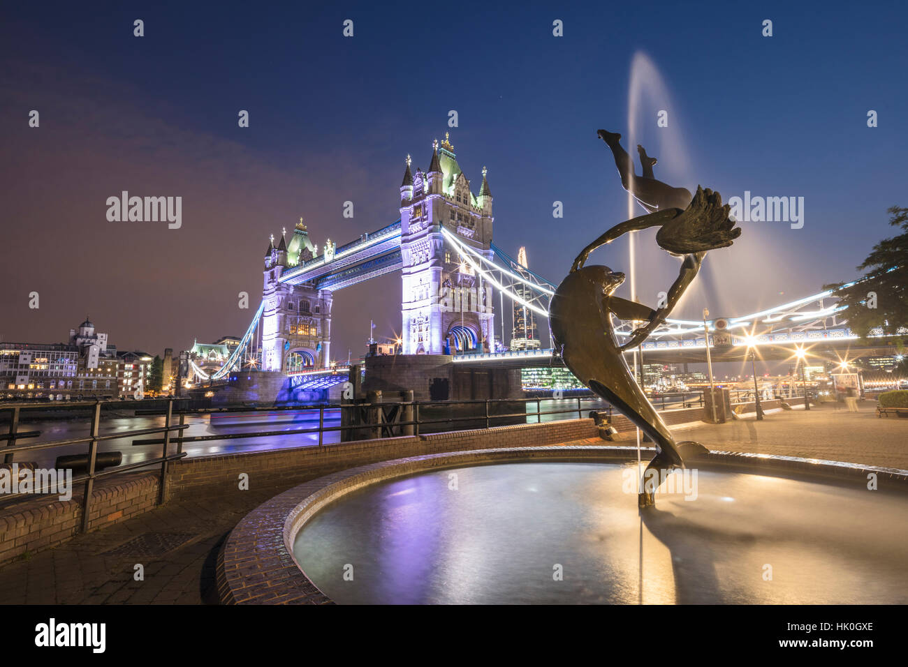 La ragazza con una fontana dei Delfini telai Tower Bridge si riflette nel fiume il Tamigi di notte, Londra, Inghilterra, Regno Unito Foto Stock