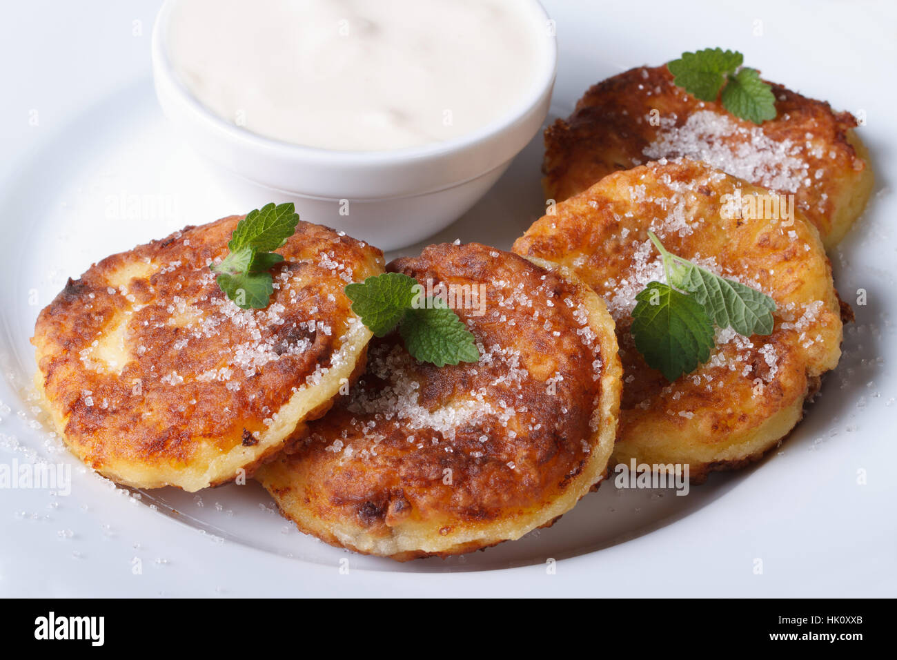 Frittelle di formaggio su una piastra bianca con panna acida closeup. una vista da sopra di un piano orizzontale Foto Stock