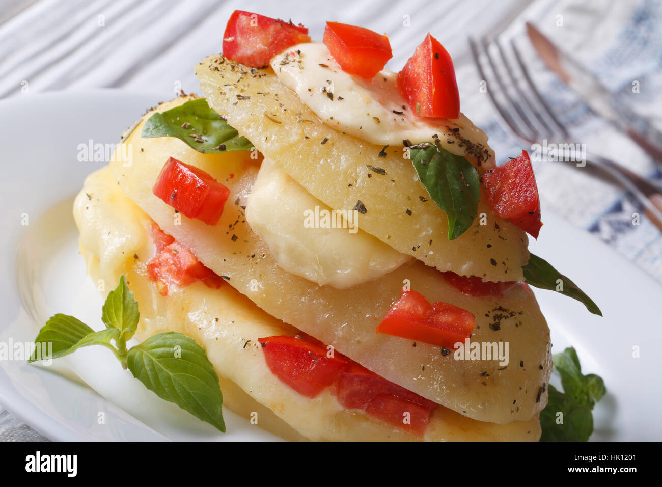 Fette di patate al forno con mozzarella, pomodoro e basilico su piastra bianca orizzontale macro Foto Stock