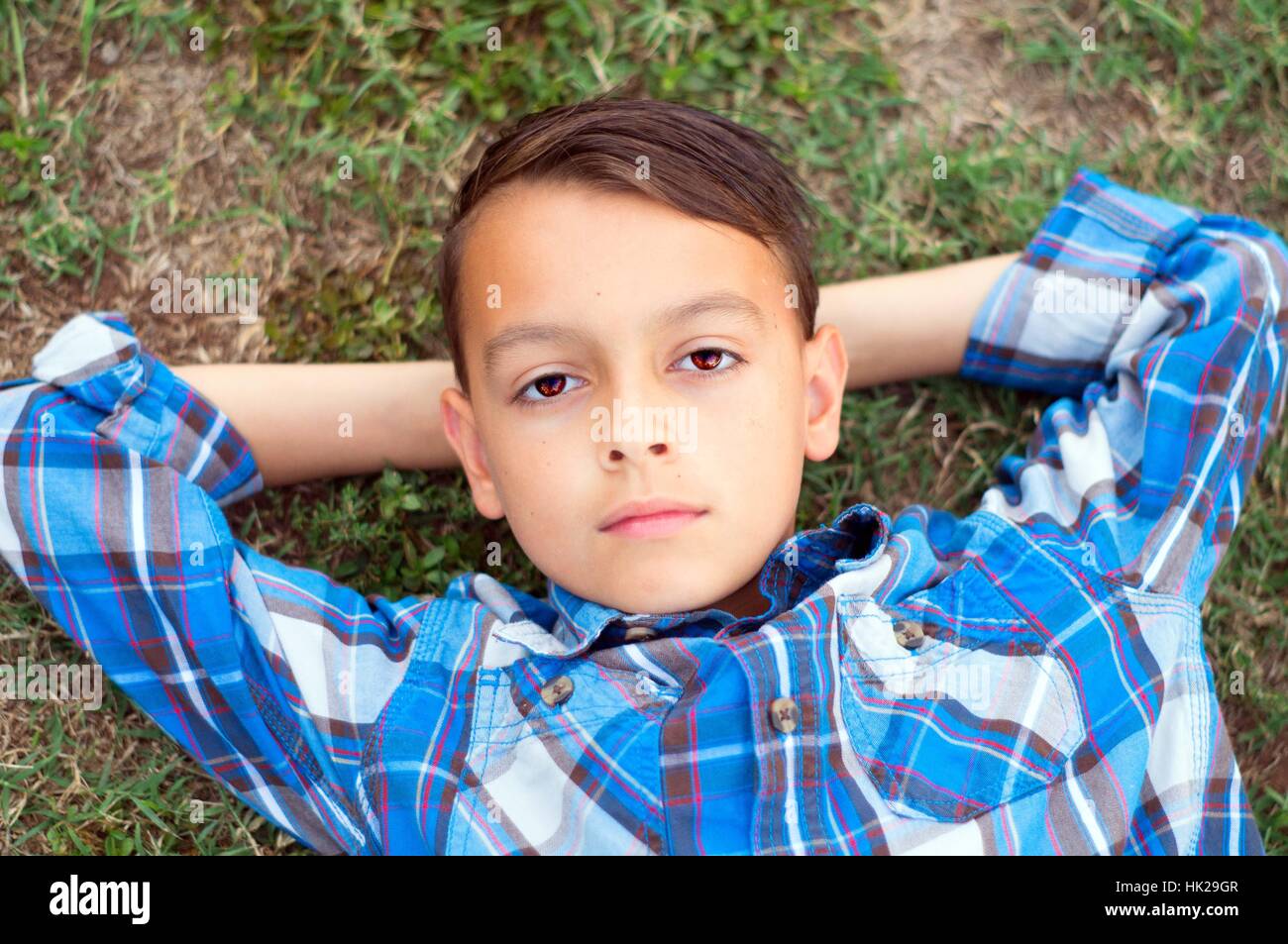 Tween boy guardando in alto nel cielo con le mani dietro la testa Foto Stock