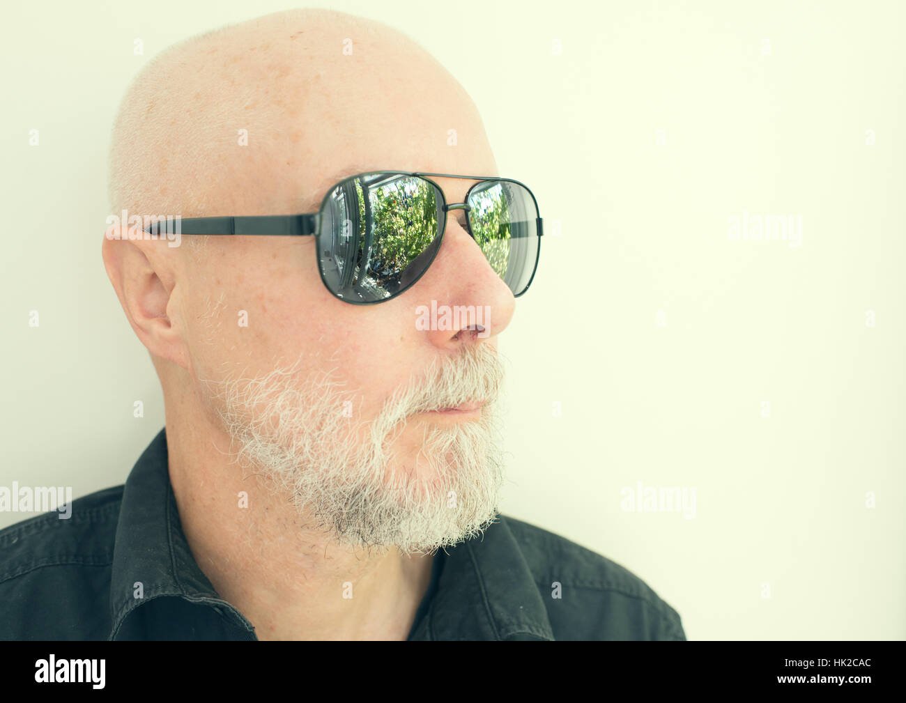 Il vecchio uomo con cool occhiali da sole guardando lontano. Giardino verde riflesse nei bicchieri. Foto Stock