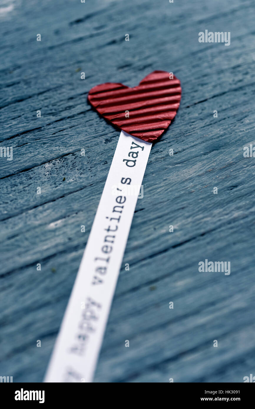 Un cuore rosso realizzato in cartone ondulato e di una striscia di carta con il testo felice il giorno di san valentino scritto in esso, su un livello di grigio rustico sfondo di legno Foto Stock